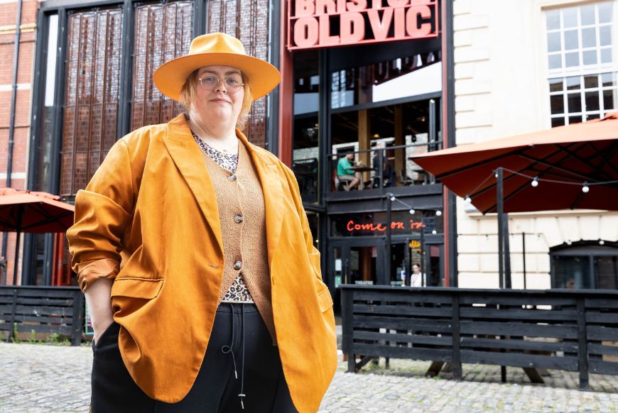 person in yellow coat and hat standing in front og bristol old vic